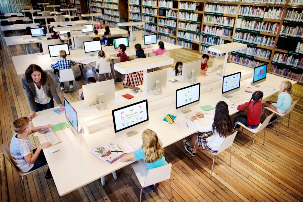 Mehrere Kinder sitzen separat an einem digitalen Arbeitsplatz in einer Schulbibliothek